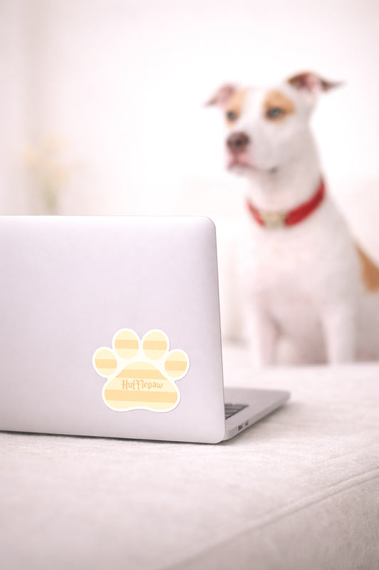Dog sitting behind a laptop with a paw print sticker on a light surface.