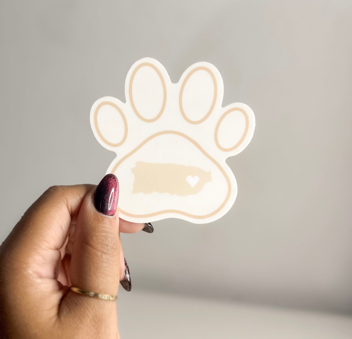 Hand holding a paw-shaped puerto rico map  sticker against a plain background