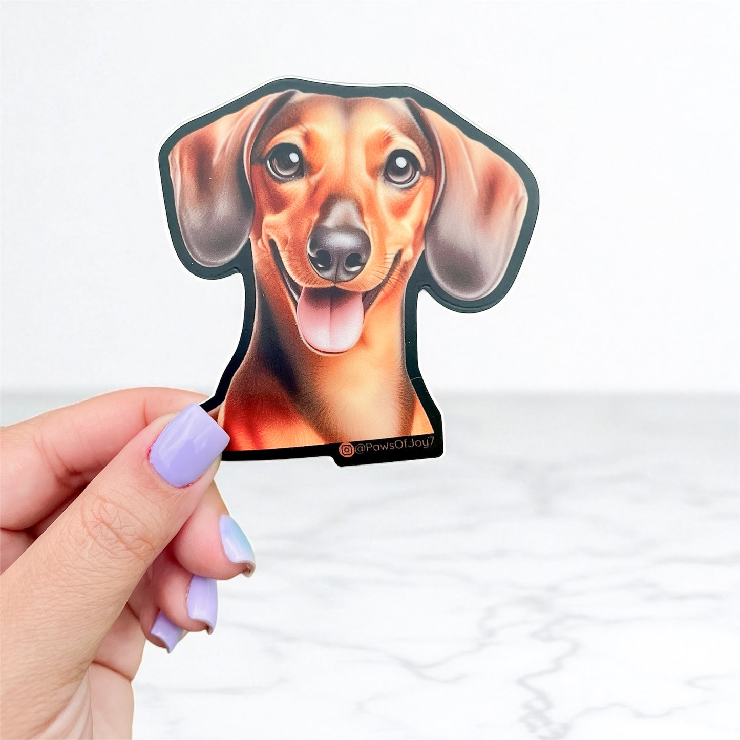 Hand holding a dachshund-shaped sticker against a white background