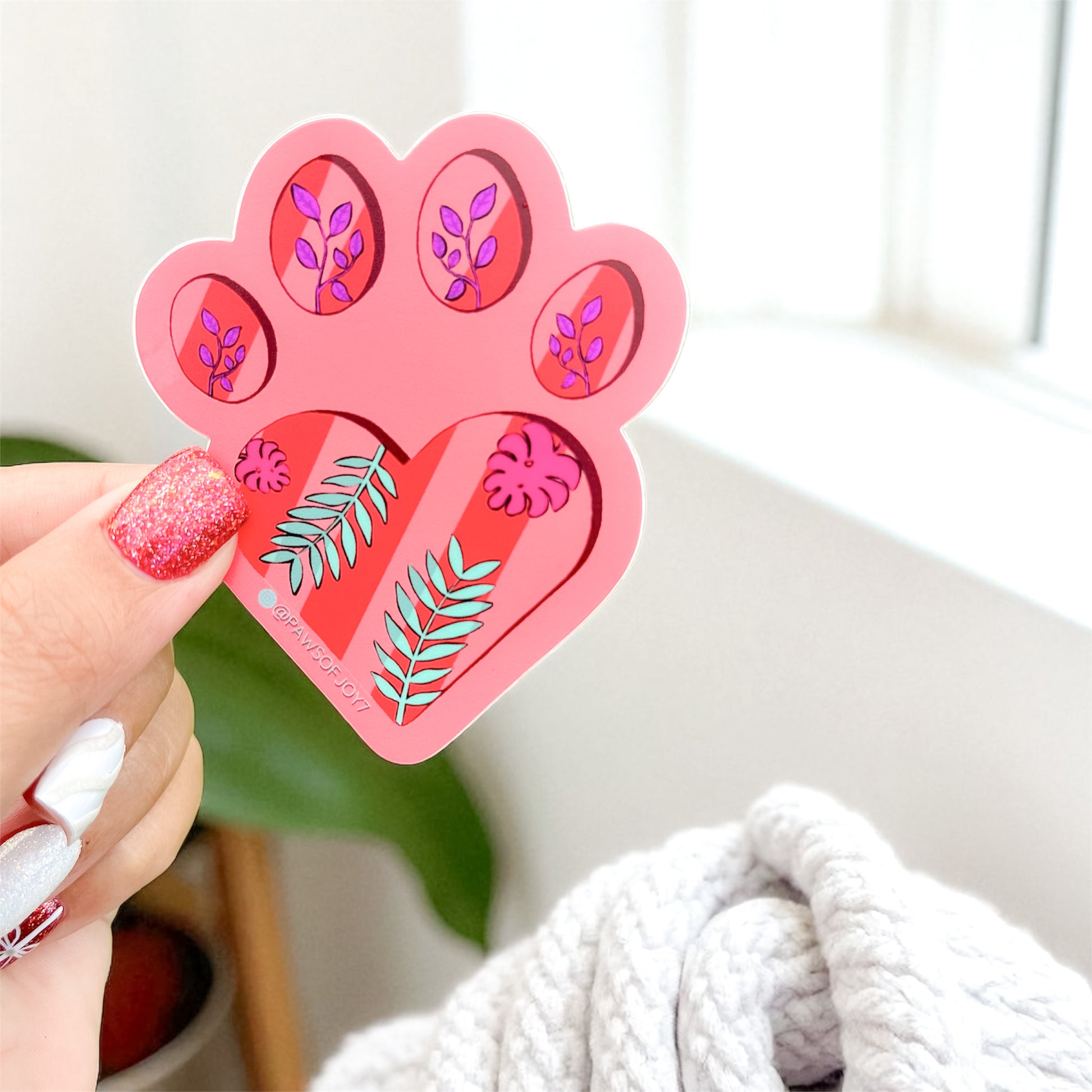 Heart-shaped pink and red decorative item with floral designs held by a hand.