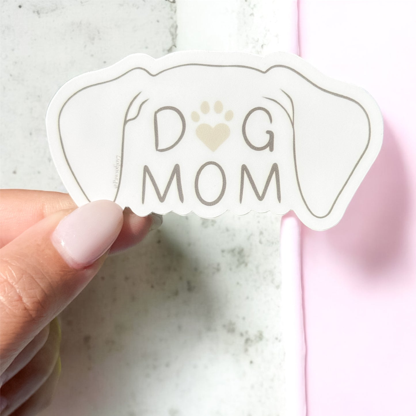 Sticker with 'DOG MOM' text held by a hand on a marble surface aesthetic
